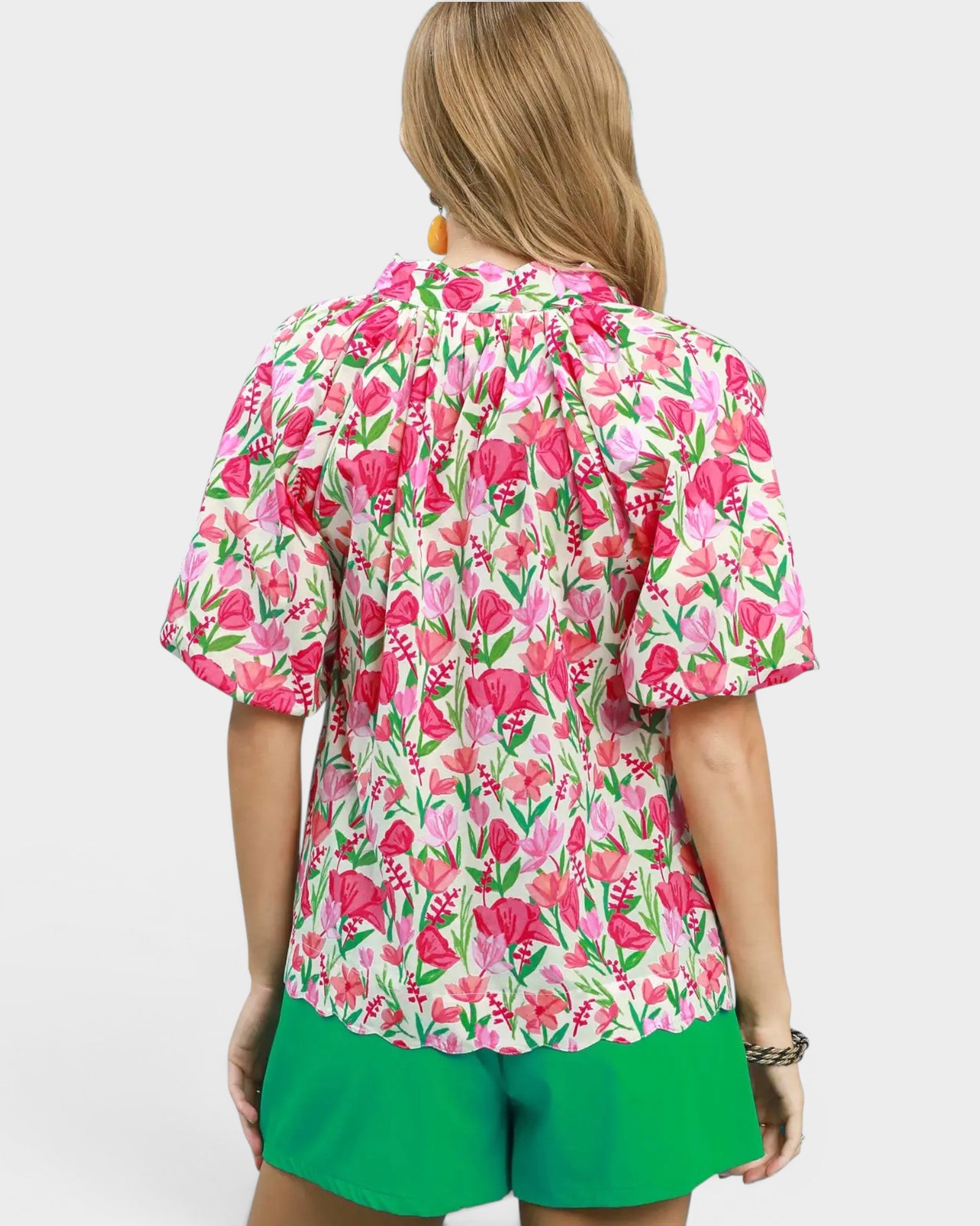 Person wearing a pink floral blouse and green shorts on a white background