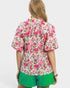 Person wearing a pink floral blouse and green shorts on a white background