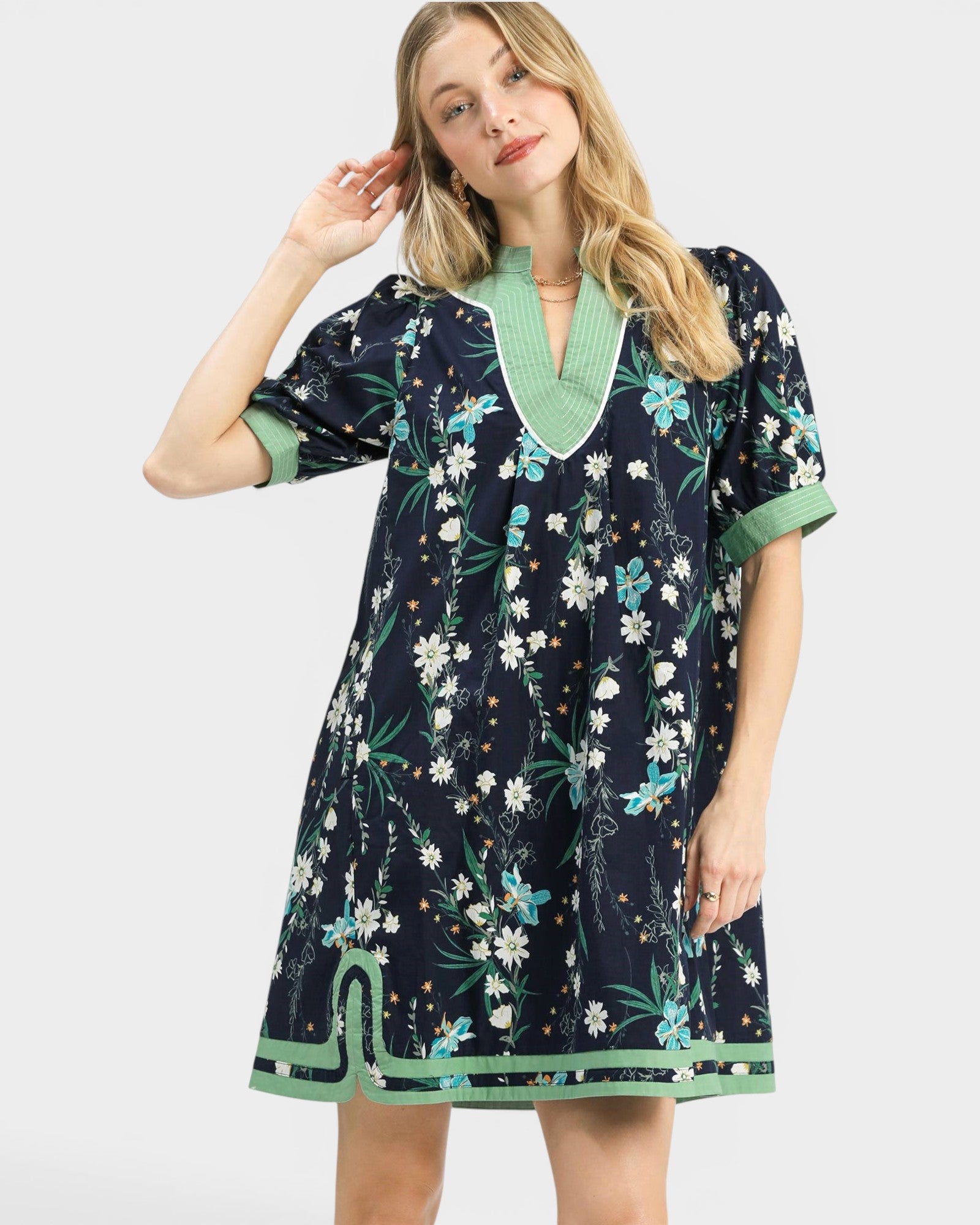 Woman wearing a navy floral dress with green trim on a white background