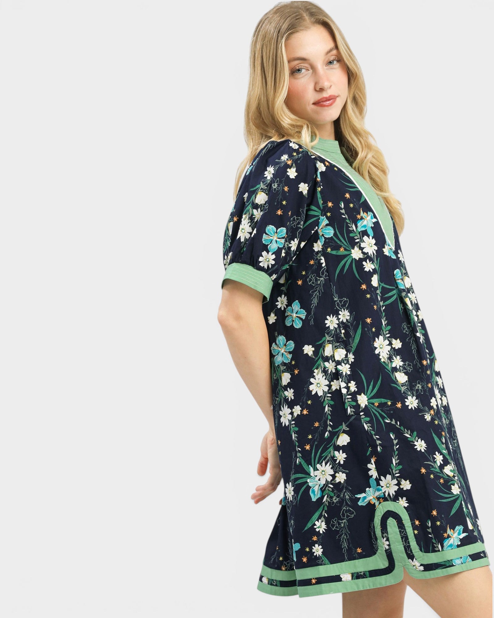 Woman wearing a navy floral dress with green trim on a white background