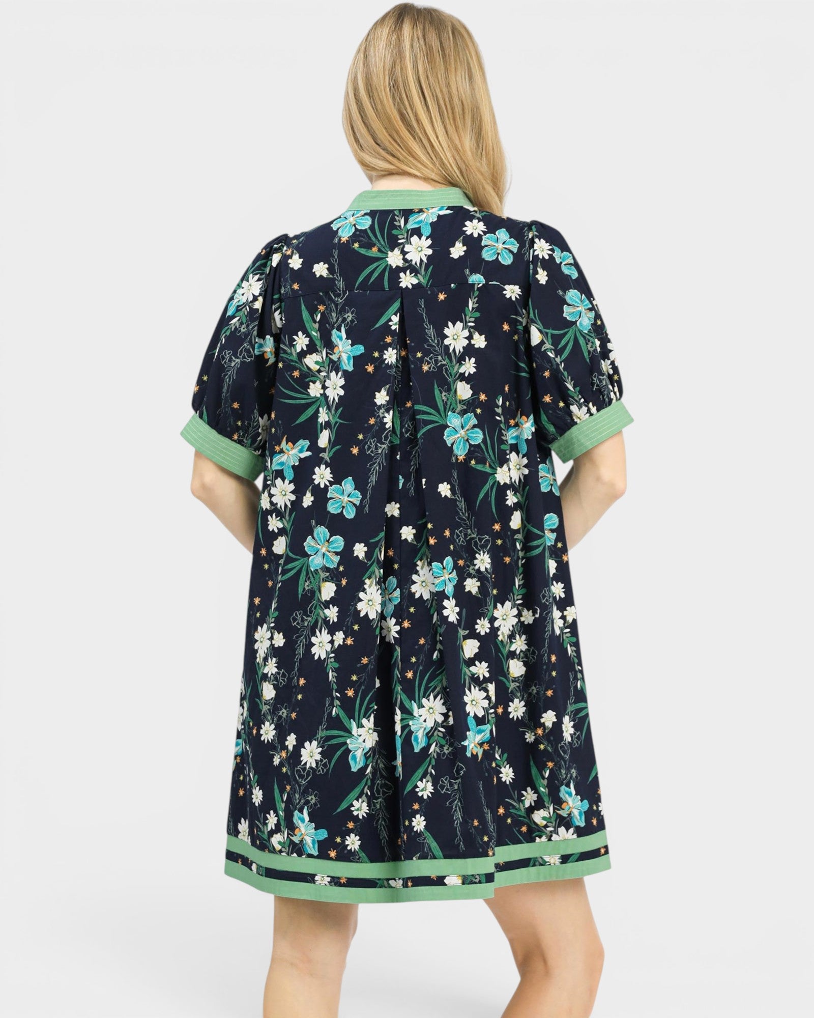 Woman wearing a navy floral dress with green trim on a white background