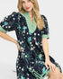 Woman wearing a navy floral dress with green accents on a white background