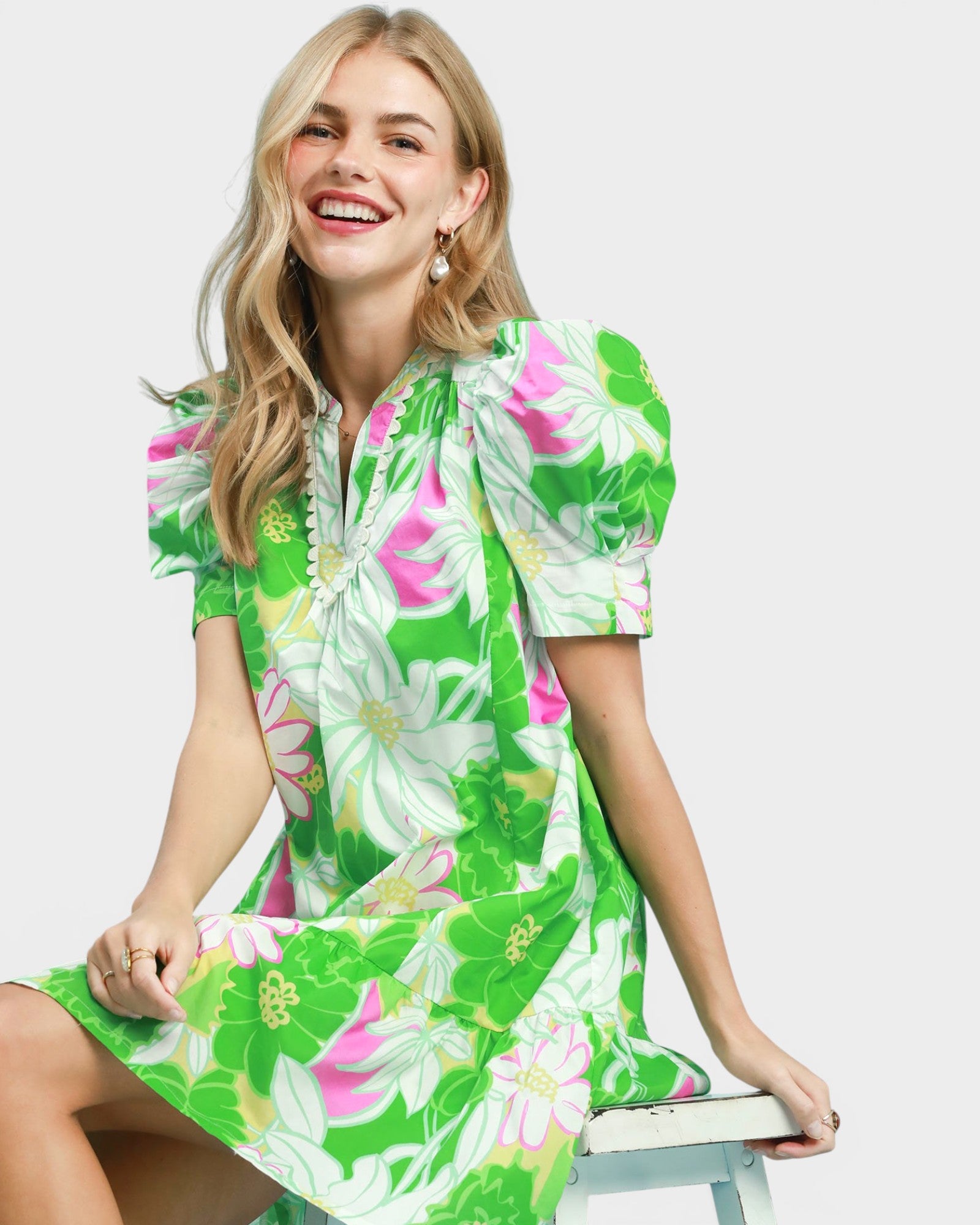 Woman wearing a green floral dress sitting on a white stool against a white background