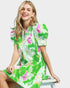 Woman wearing a green floral dress sitting on a white stool against a white background