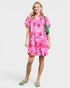 Woman wearing a pink floral dress with a green bag on a white background