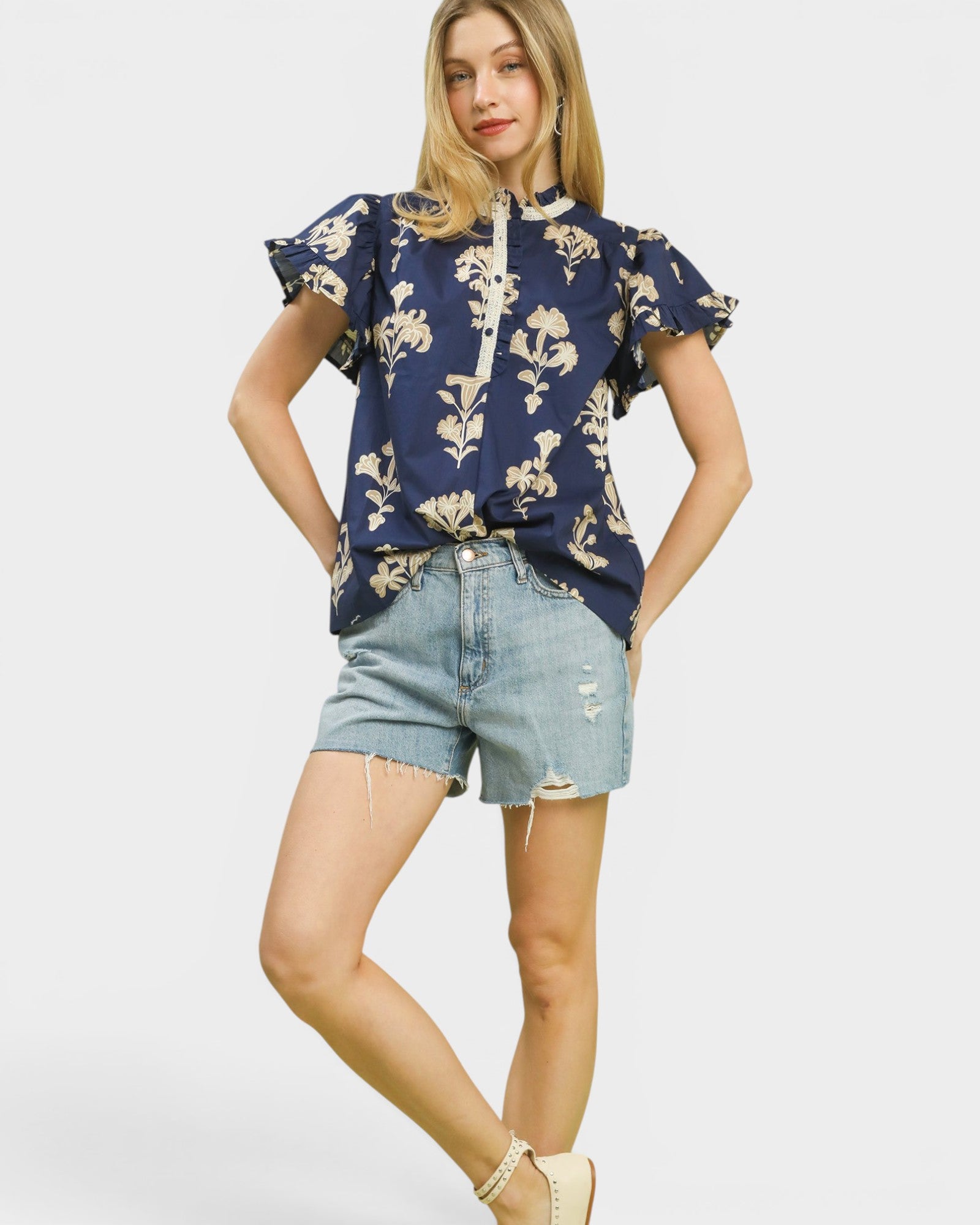 Woman wearing a navy floral blouse and denim shorts on a white background
