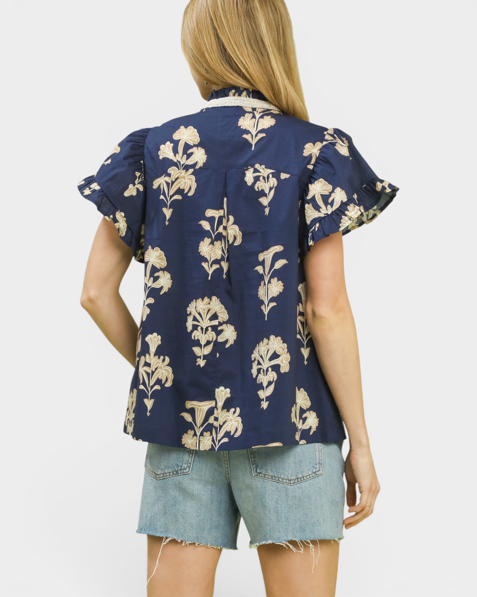 Woman wearing a navy blue floral patterned shirt and denim shorts on a white background