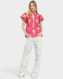 Person wearing a pink floral blouse and white pants on a white background