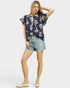 Woman wearing a navy floral top and denim shorts on a white background