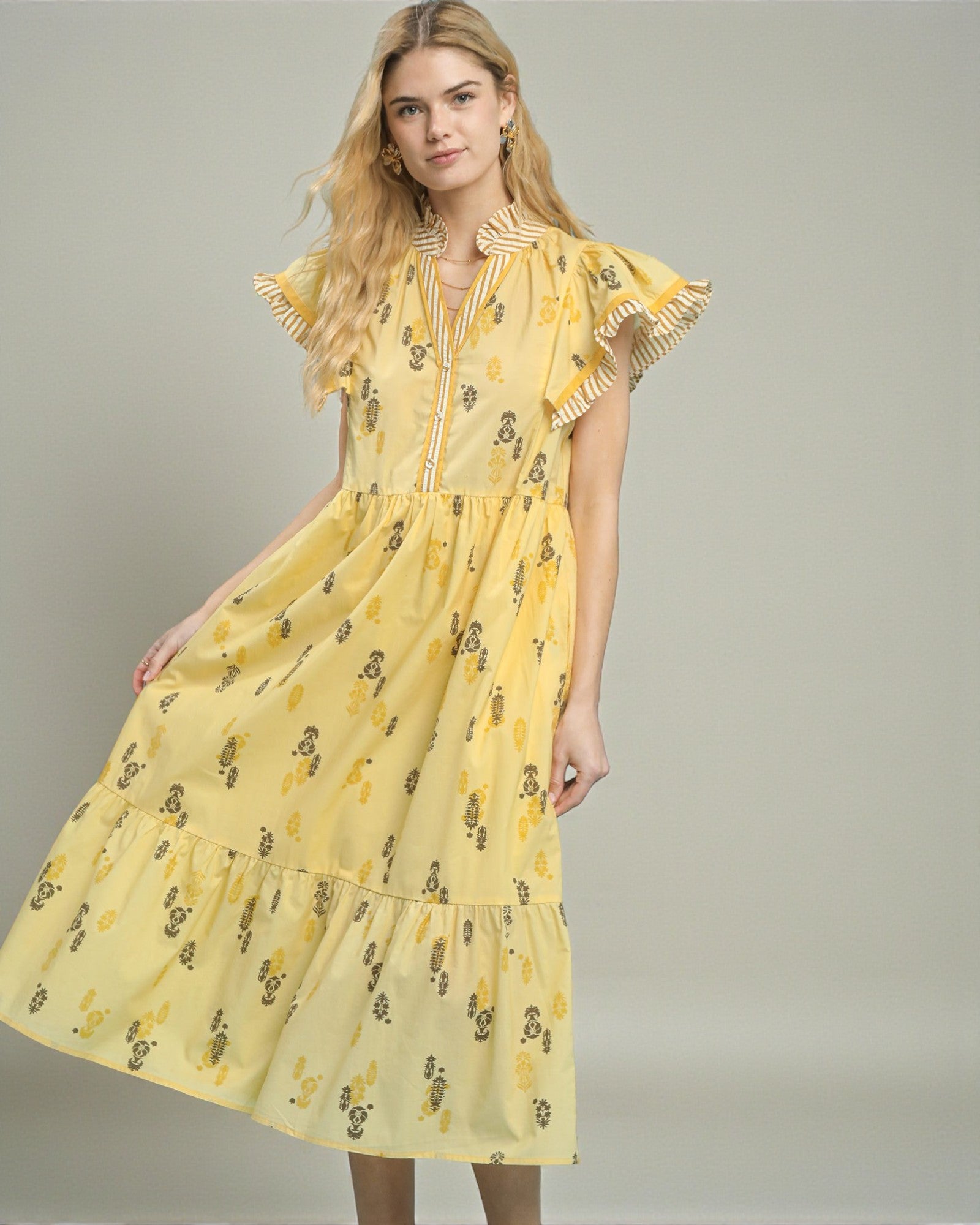 Woman wearing a yellow dress with a floral pattern on a plain background