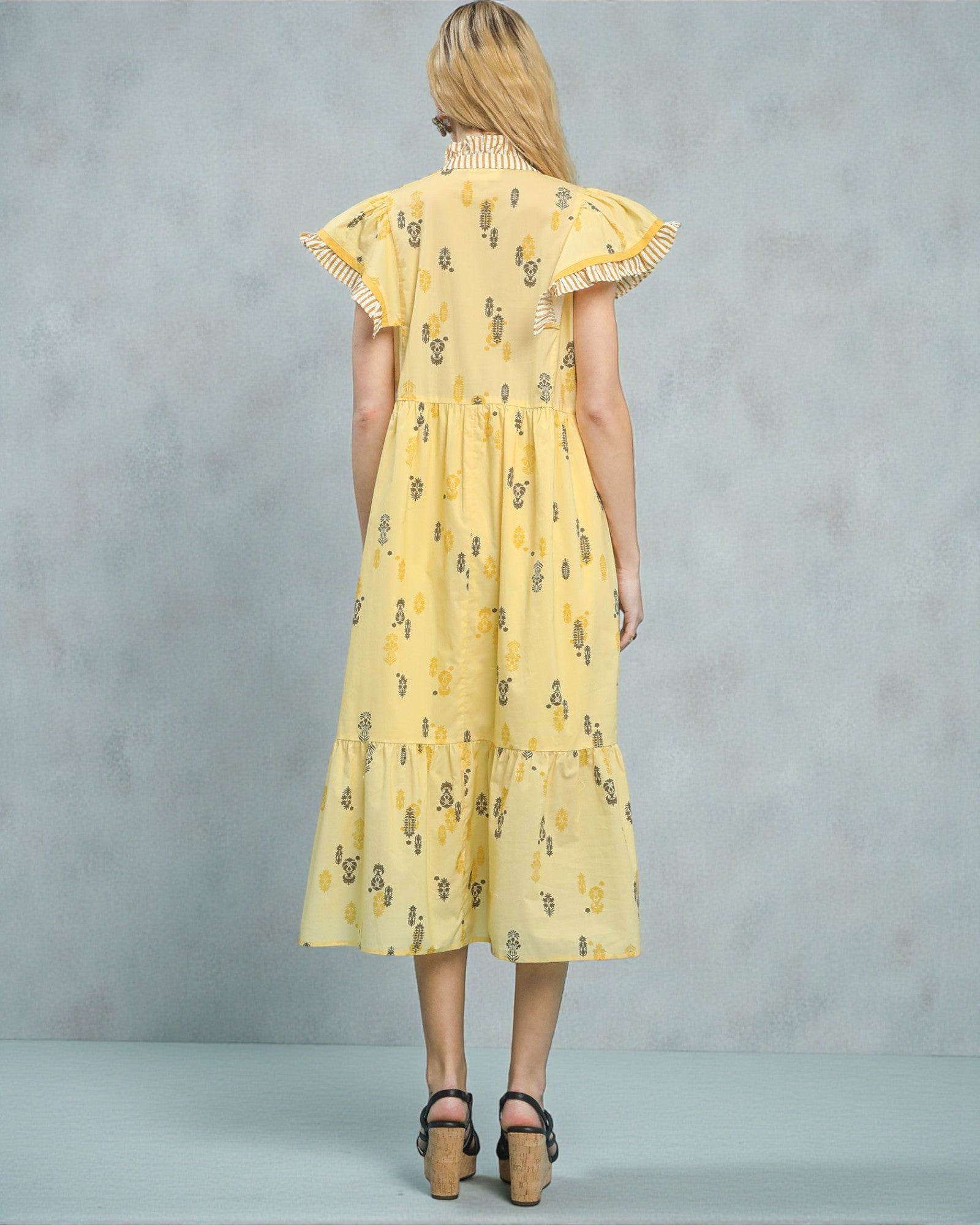 Woman wearing a yellow dress with floral pattern against a gray background
