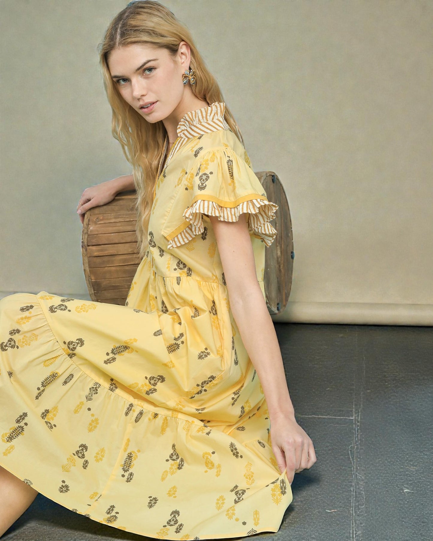 Woman wearing a yellow dress with a floral pattern, sitting on a wooden chair.