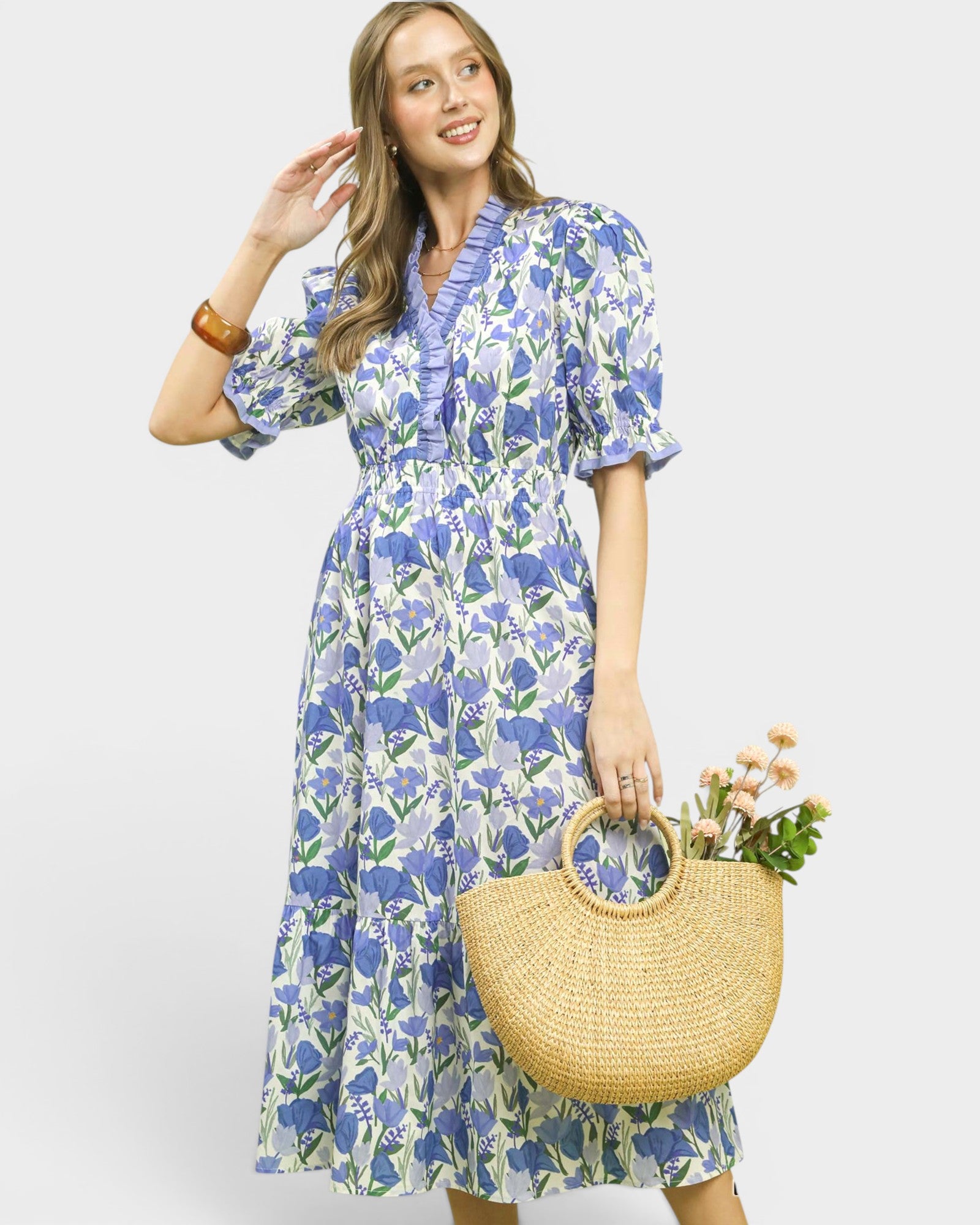 Woman wearing a blue floral dress holding a straw bag with flowers on a white background