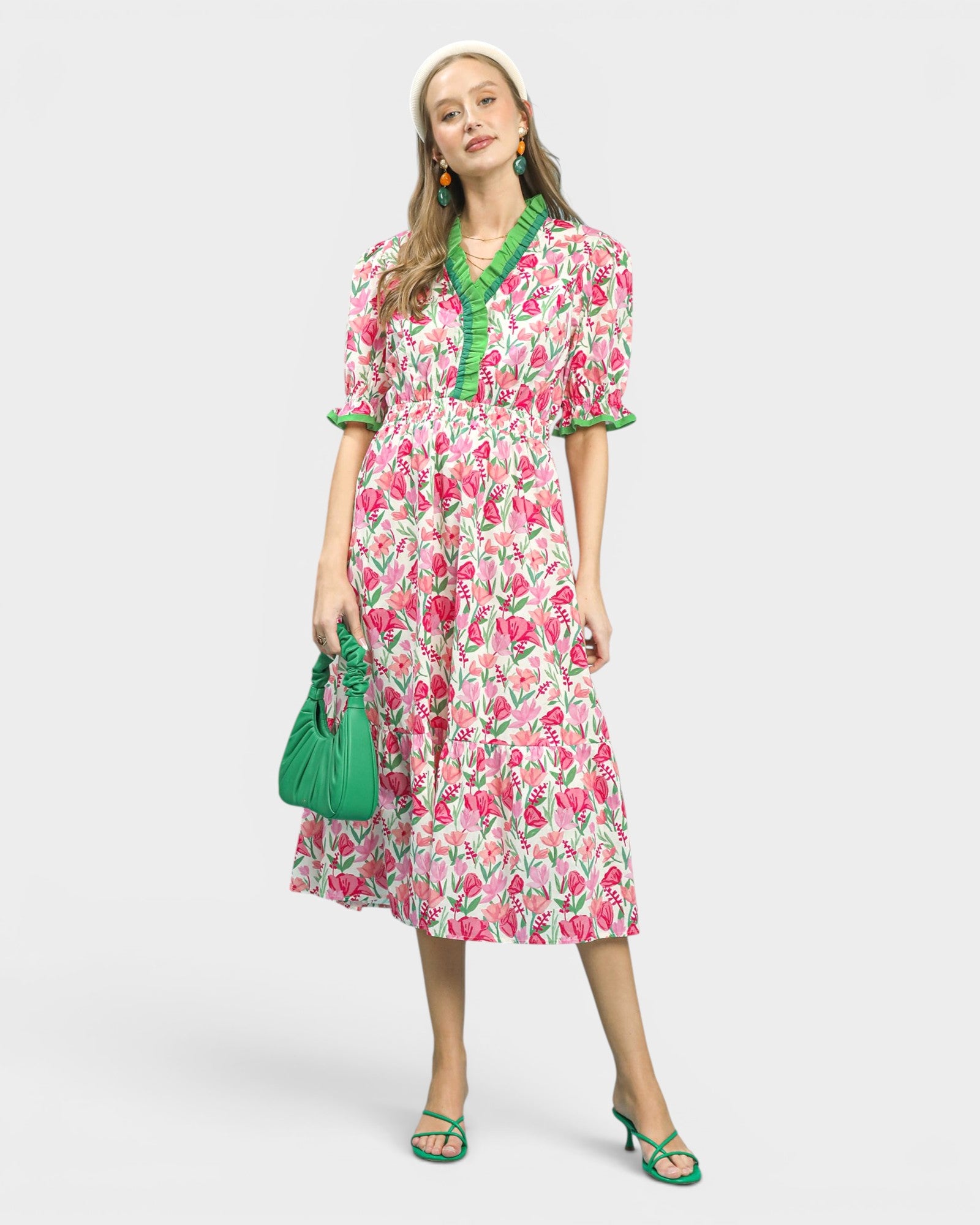 Woman wearing a floral dress with green accents and holding a green handbag on a white background