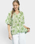 Woman wearing a green patterned blouse and white pants on a light gray background