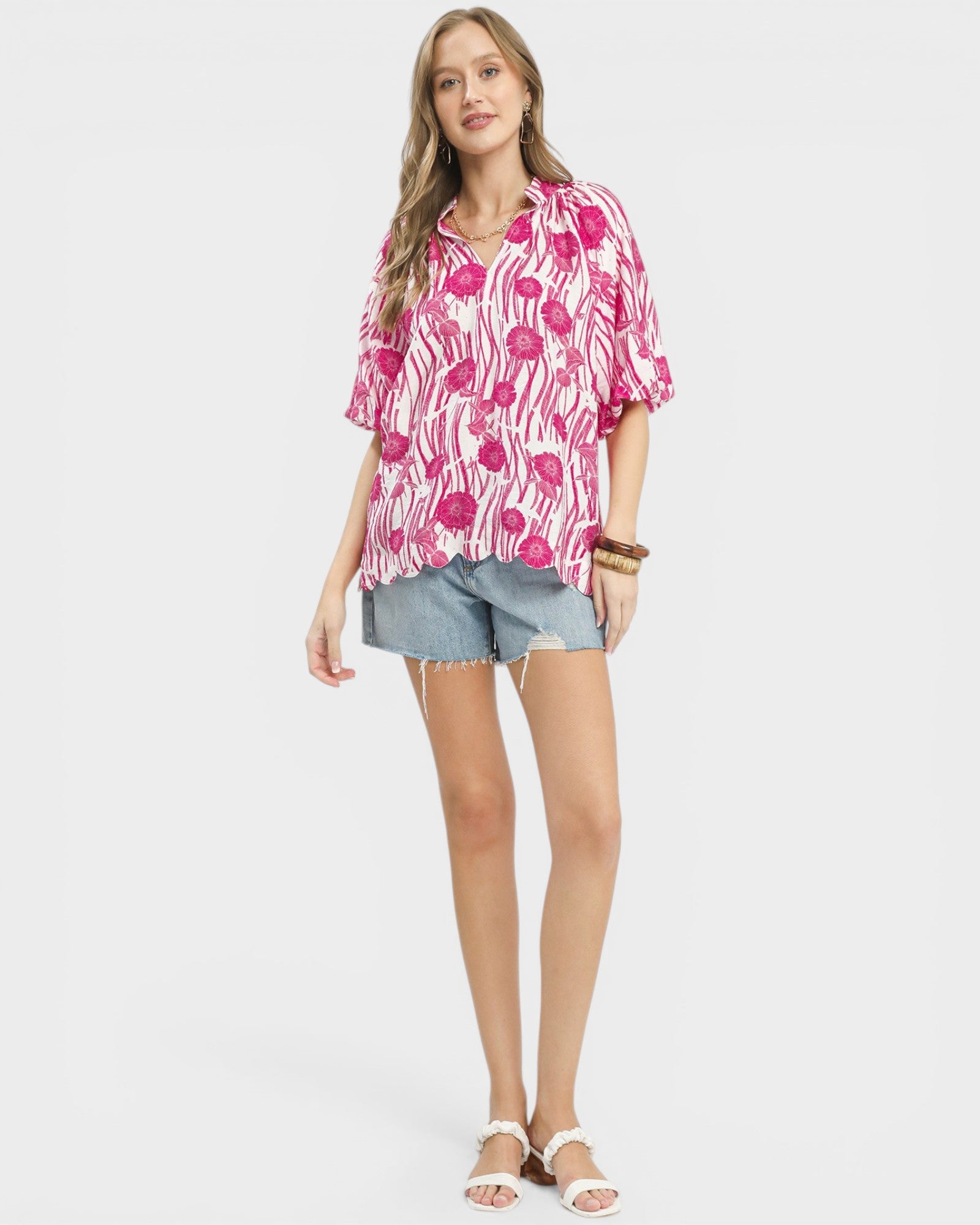 Woman wearing a pink patterned blouse and denim shorts on a white background
