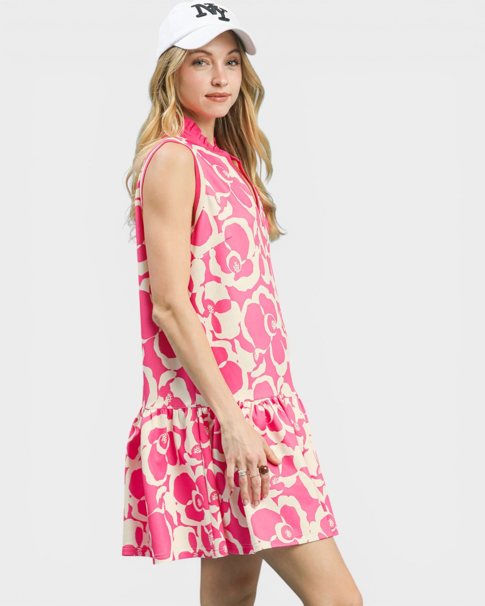 Woman wearing a pink floral dress and white cap on a plain background