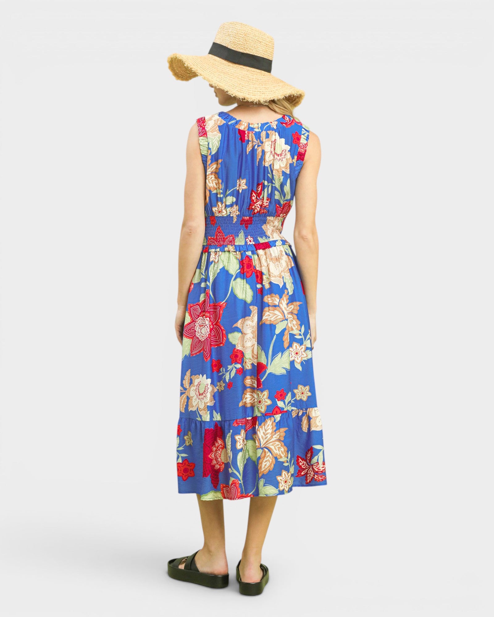Person wearing a colorful floral dress and straw hat on a white background