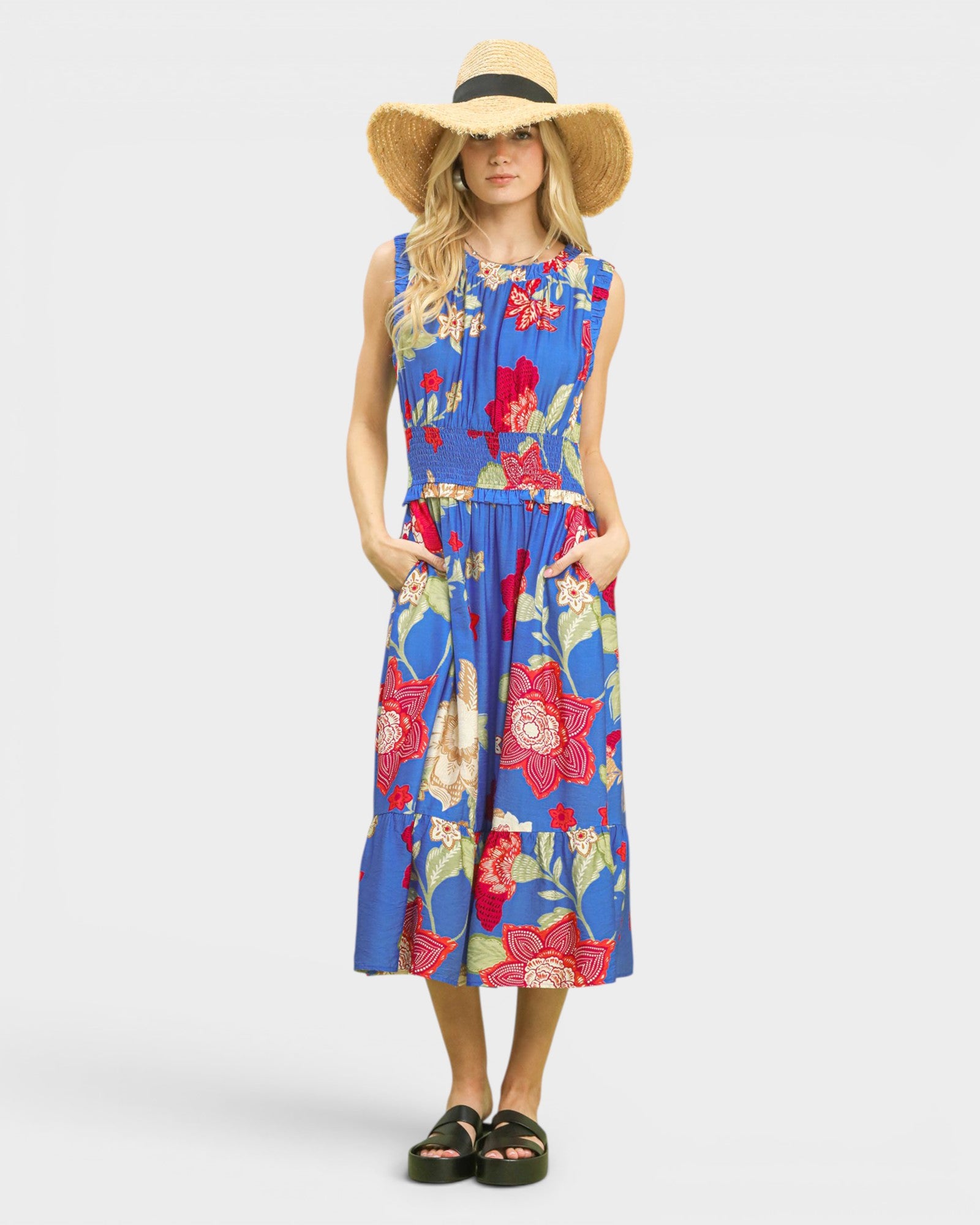 Woman wearing a colorful floral dress with a wide-brimmed hat on a white background