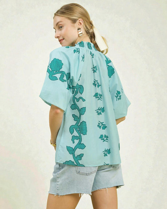 Woman wearing a light blue kimono-style top with green floral patterns on a plain background
