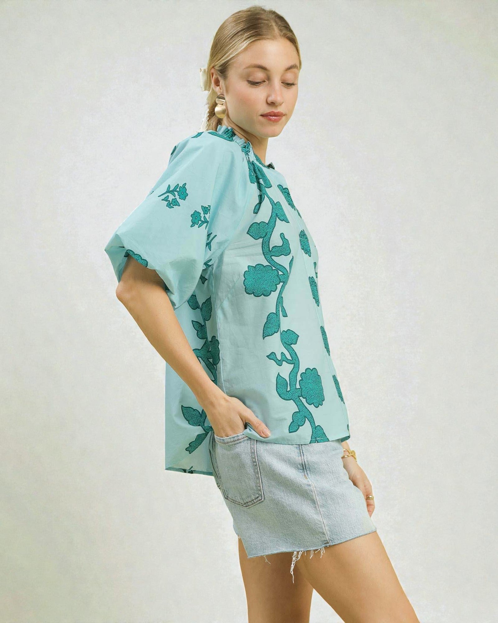 Woman wearing a light blue floral blouse and denim shorts on a white background