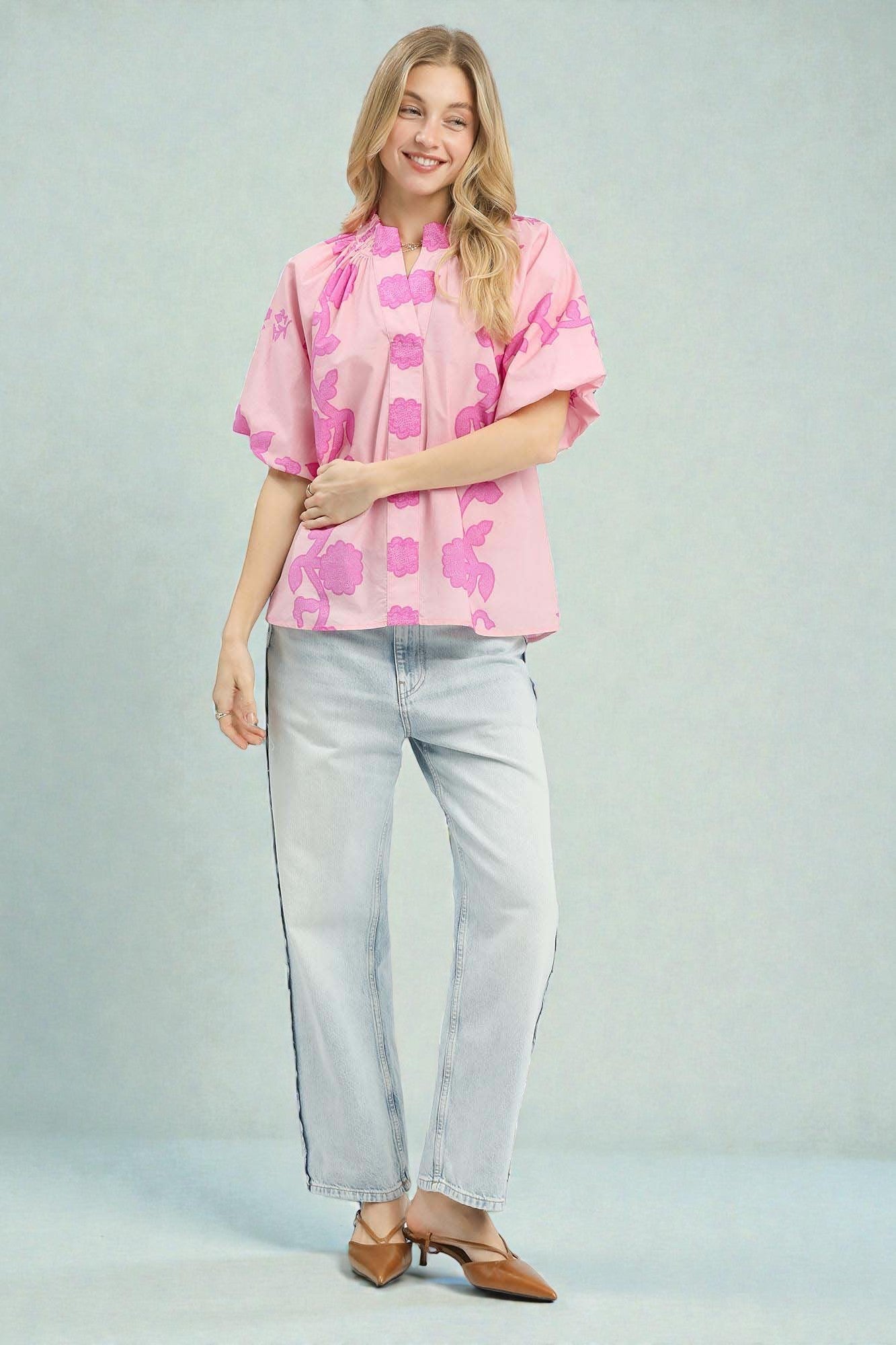 Woman wearing a pink floral blouse and light blue jeans on a gray background