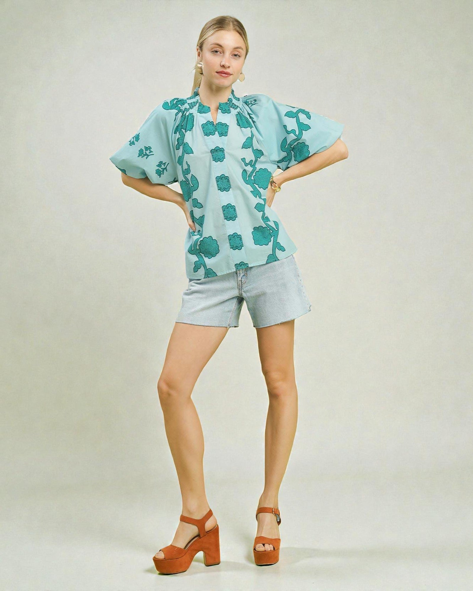 Woman wearing a light blue floral blouse and shorts on a plain background