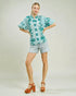 Woman wearing a light blue floral blouse and shorts on a plain background
