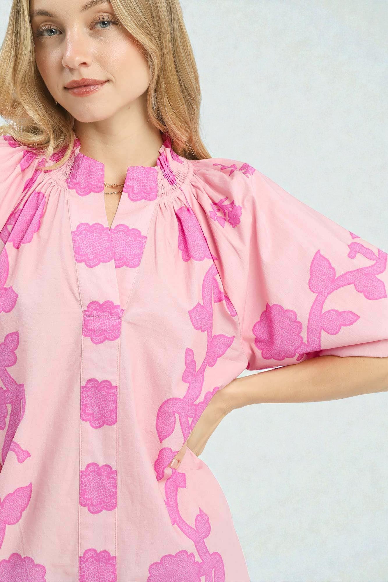 Woman wearing a pink dress with floral patterns on a plain background