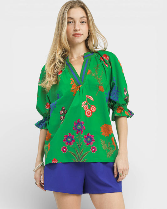 Woman wearing a green embroidered blouse with colorful floral patterns on a white background