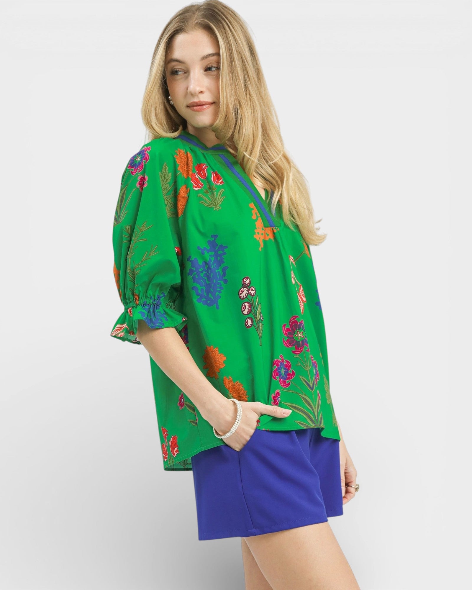 Woman wearing a green floral embroidered top with blue shorts on a white background
