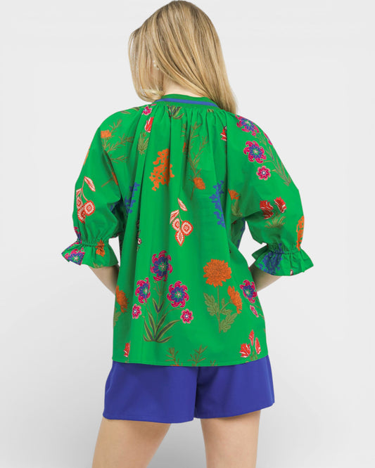 Person wearing a green blouse with colorful floral patterns and blue shorts on a white background