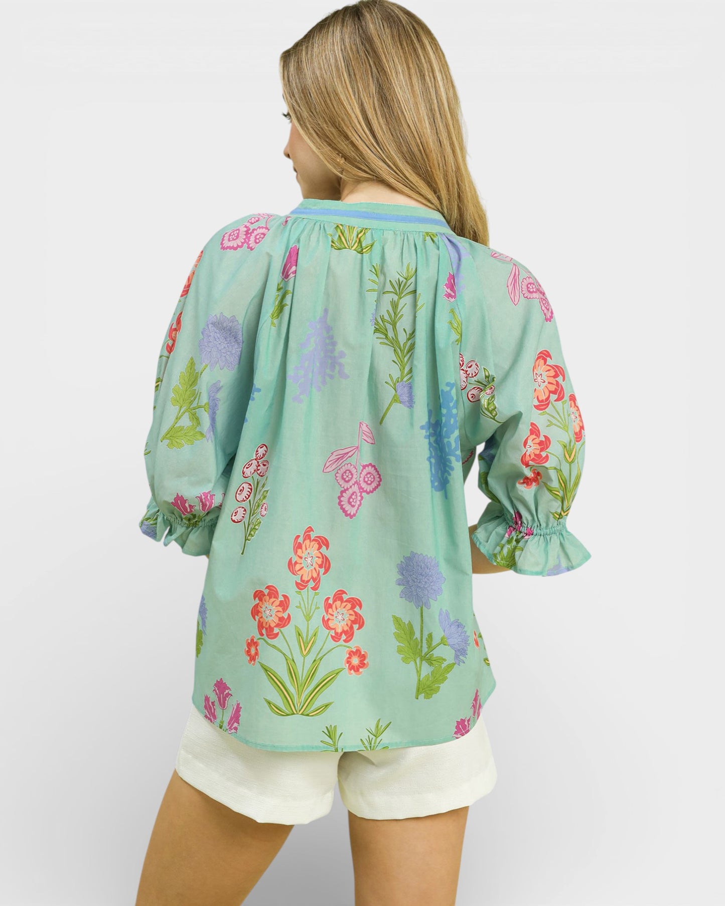 Woman wearing a light blue floral blouse with white shorts on a plain background
