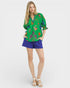 Woman wearing a green embroidered blouse and blue shorts on a white background