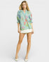 Woman wearing a light blue floral blouse and white shorts on a white background