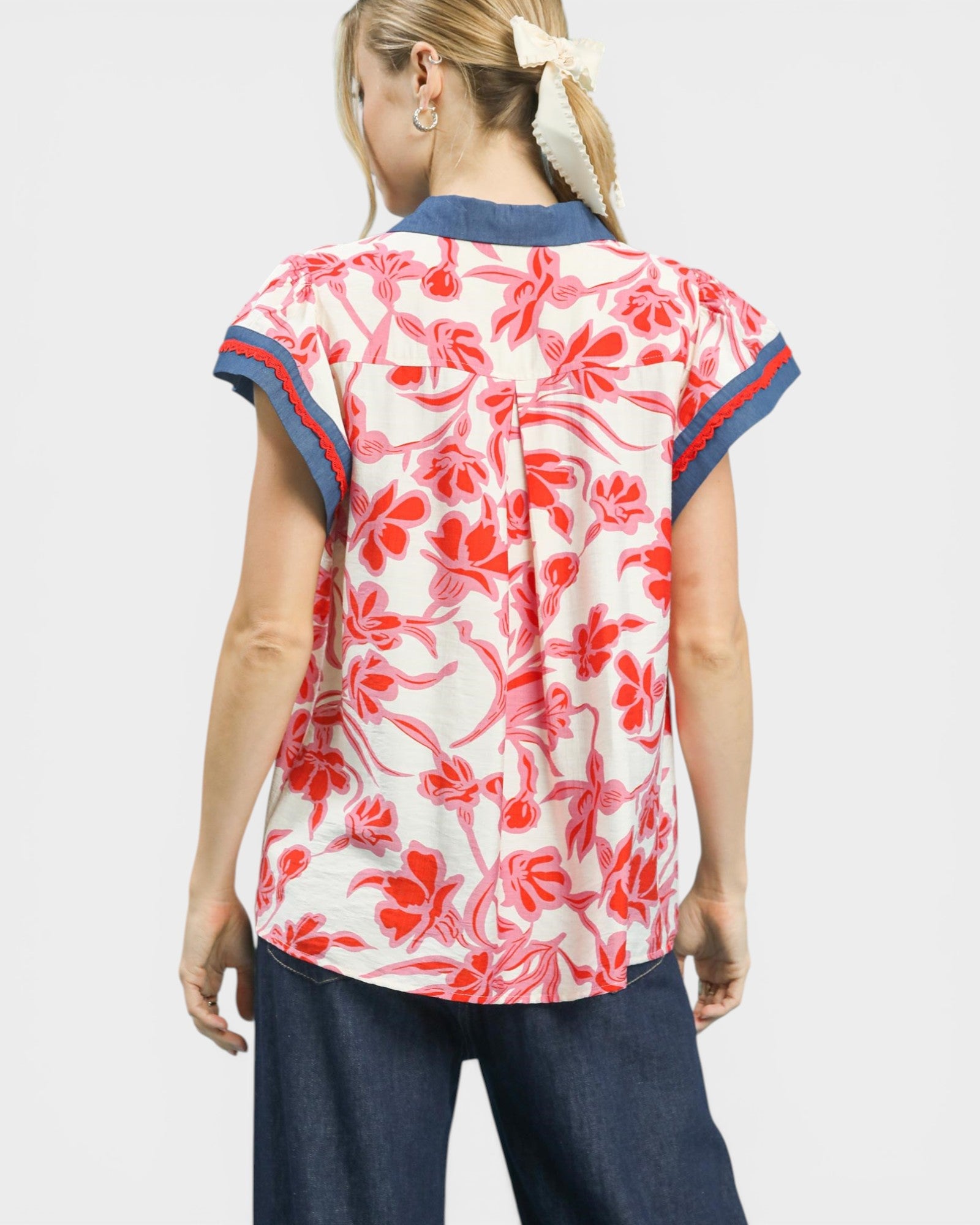 Woman wearing a red and white floral blouse with blue accents on a plain background