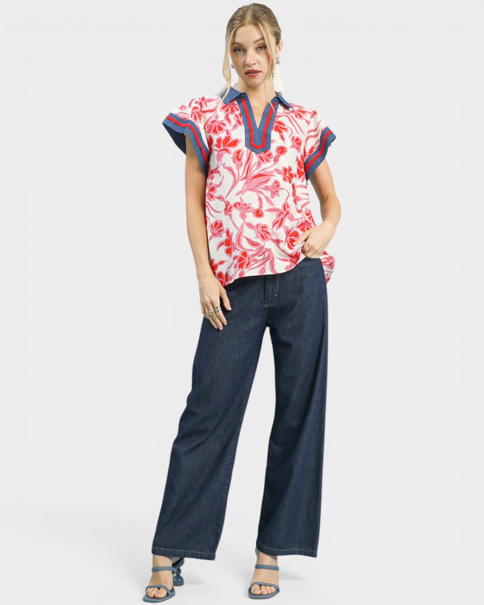 Woman wearing a floral blouse with red and blue trim and wide-leg jeans on a white background