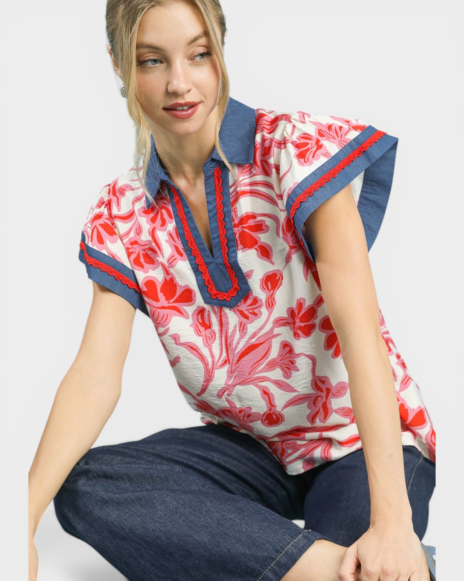 Woman wearing a red and white floral blouse with blue accents on a plain background
