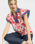 Woman wearing a red and white floral blouse with blue accents on a plain background