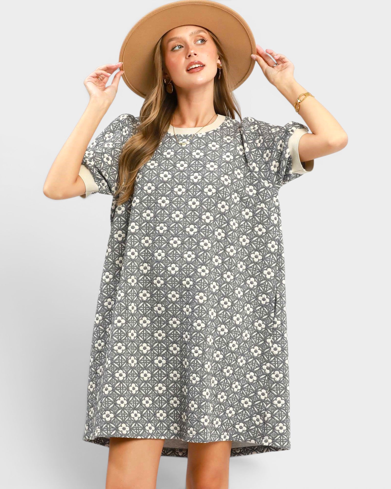 Woman wearing a gray floral dress and beige hat on a light gray background