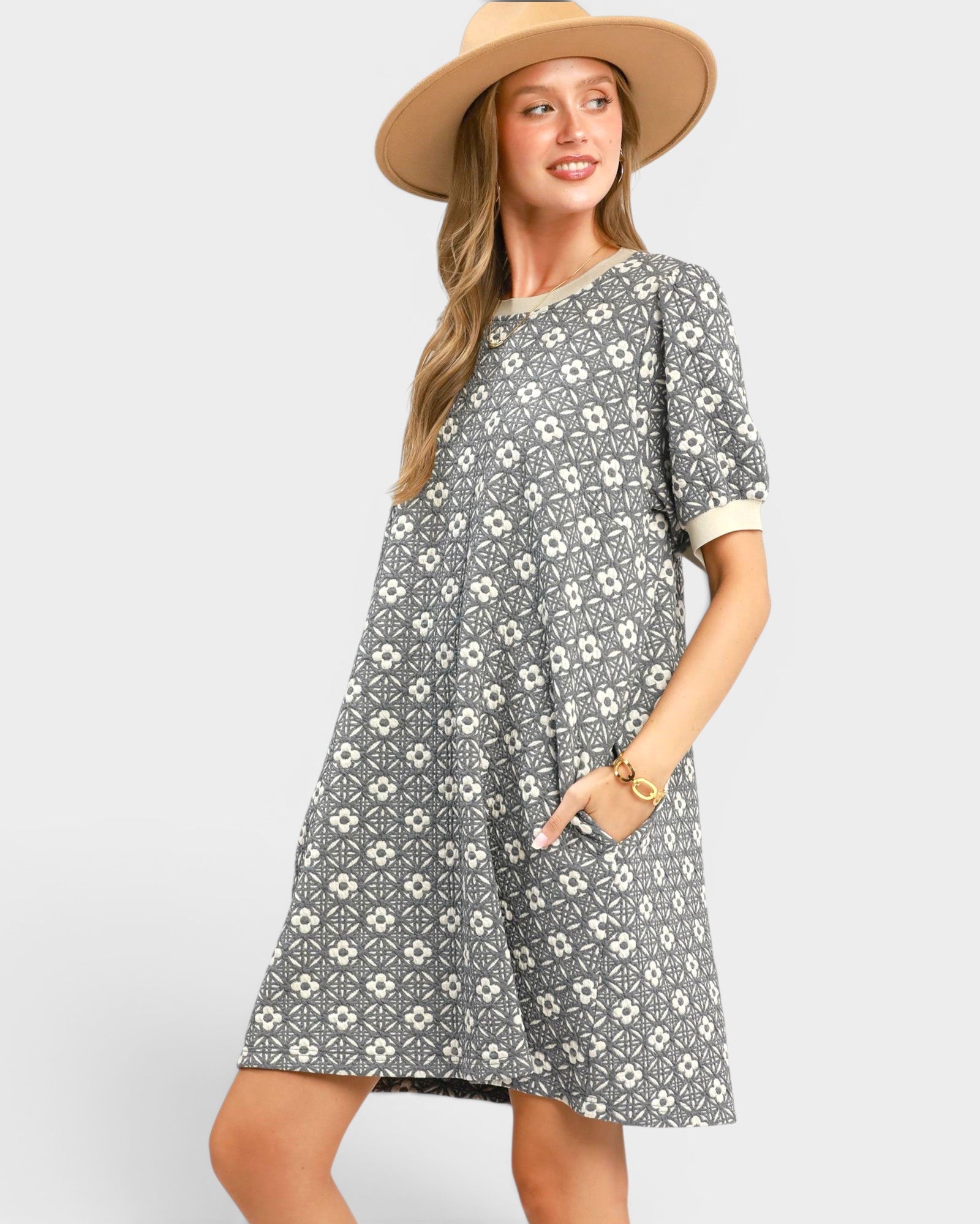 Woman wearing a gray floral dress and beige hat on a white background