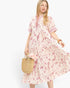 A woman modeling a short-sleeve midi dress with a pink and red abstract floral print on a cream background.