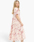 A woman modeling a short-sleeved midi dress with a pink and white floral pattern, photographed against a solid light gray background.
