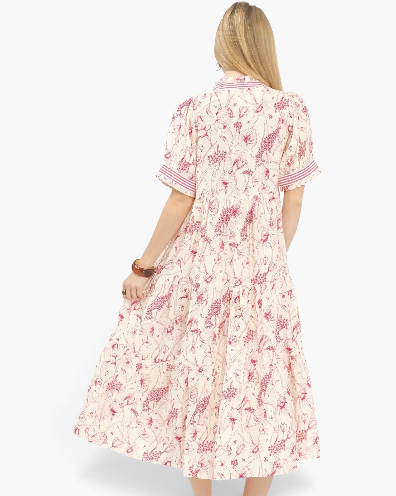 A woman viewed from the back wearing a short-sleeve midi dress with a pink and red botanical print on a cream background, set against a plain white studio background.