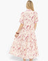 A woman viewed from the back wearing a short-sleeve midi dress with a pink and red botanical print on a cream background, set against a plain white studio background.