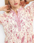 A woman modeling a short-sleeve midi dress with a pink and red abstract floral print on a cream background.