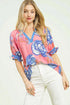 Woman wearing a pink floral blouse with white pants on a light background