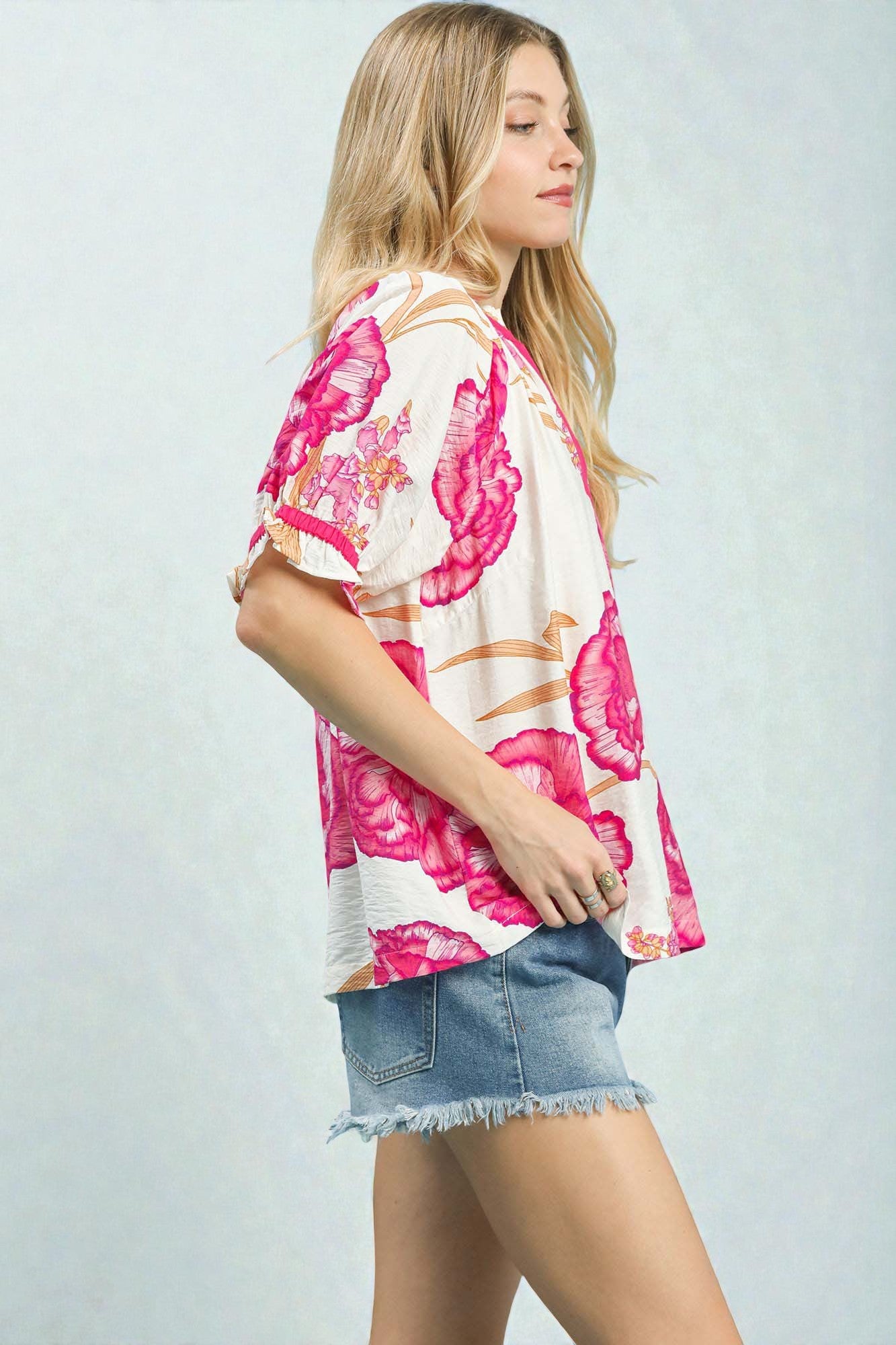 Woman wearing a floral kimono-style top and denim shorts on a light gray background