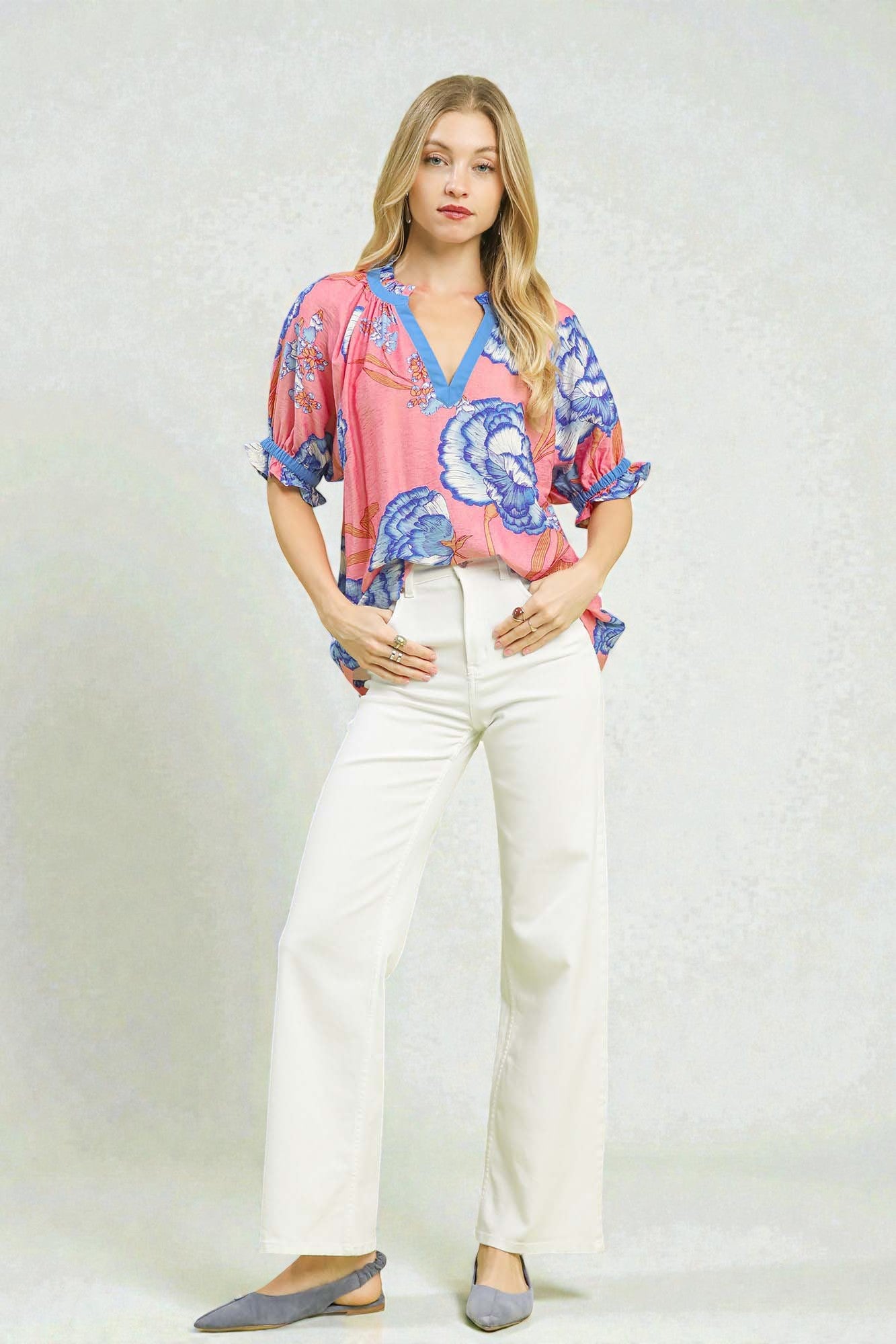 Woman wearing a colorful blouse and white pants on a plain background