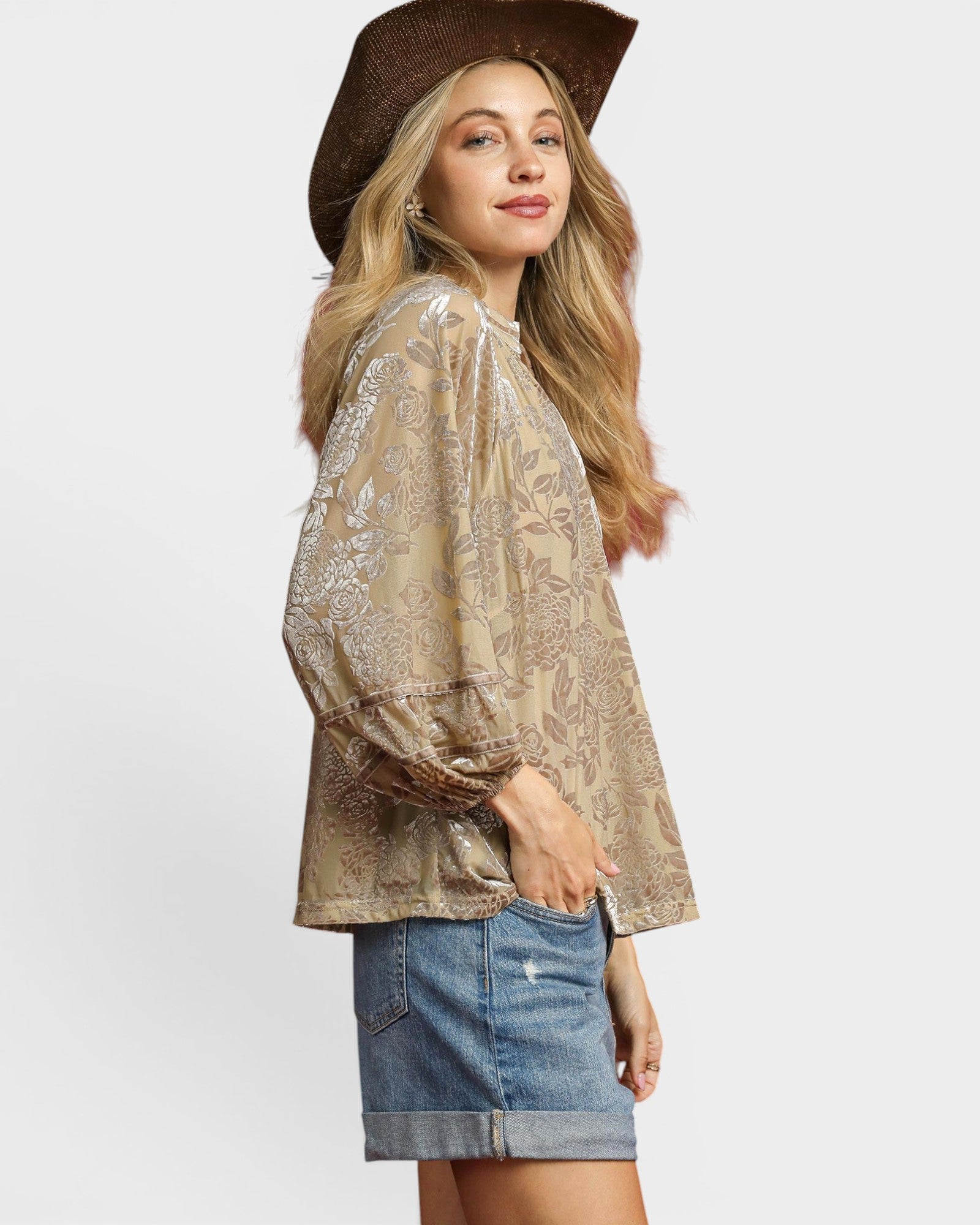 Woman wearing a beige lace blouse and denim skirt with a brown hat on a white background